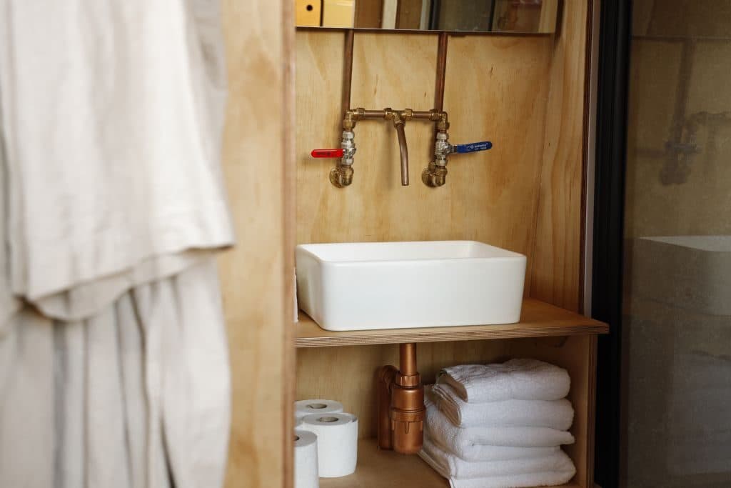 A ceramic basin with exposed copper taps and folded white towels in the plywood bathroom.