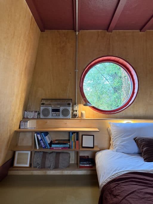 The built-in bed beneath a round porthole window onto green trees, with a cassette player on the shelf.