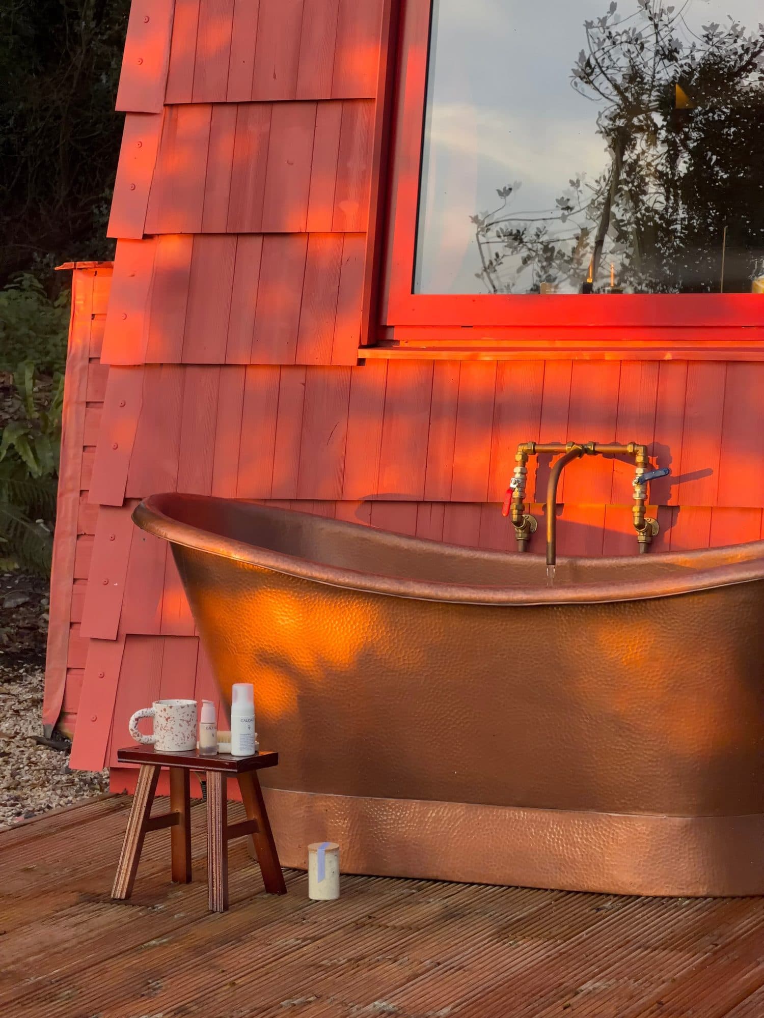 A hammered copper bath on the deck against Cucu's red-shingled wall, lit by evening sun.