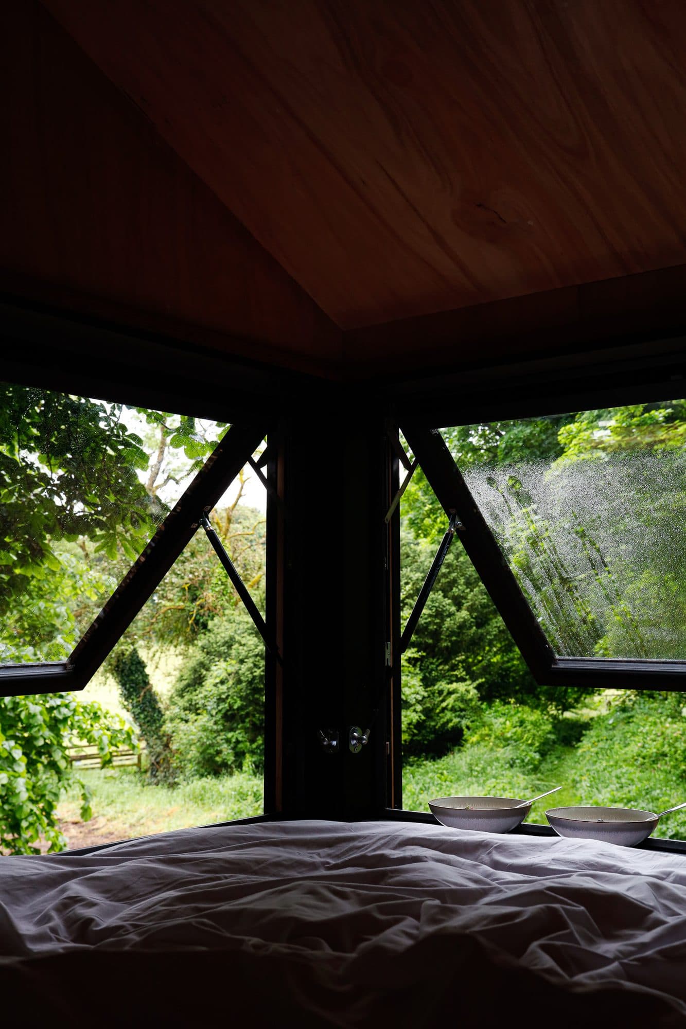 The bed inside Saoirse, with the wide window propped open onto green woodland.