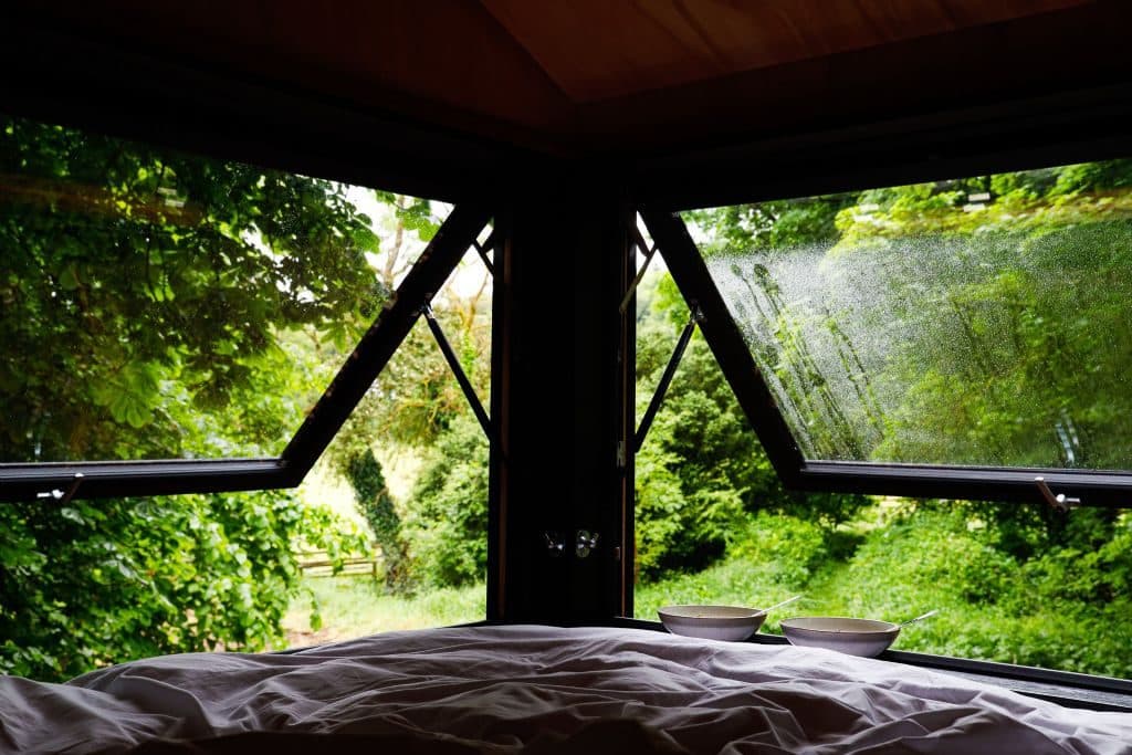 The corner picture windows framing the forest from the foot of the bed.