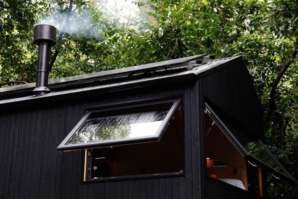 The cabin's window swung open beneath the trees, smoke rising from the stove's chimney.
